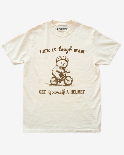'Life Is Tough Man Get Yourself A Helmet' shirt in ivory with a retro graphic of a little bear riding a bycicle.