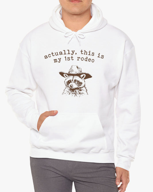 Man wearing an 'Actually, This is My First Rodeo' hoodie in white, featuring a retro western graphic design and unisex fit.