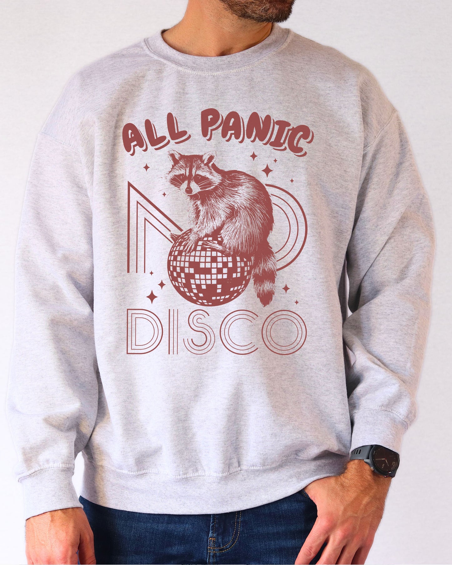 Man wearing an ash gray sweatshirt featuring a funny retro raccoon sitting on a disco ball graphic and the quote 'All Panic No Disco'.