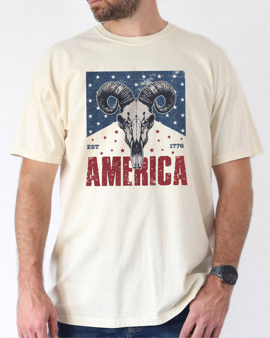 Model wearing natural color shirt with 'America Est 1776' graphic design
