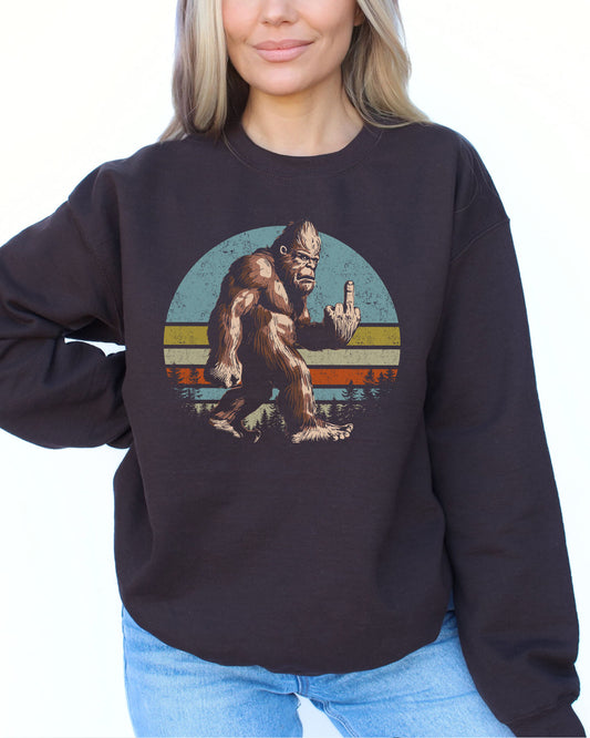 Woman wearing a dark chocolate color sweatshirt featuring a funny retro-style Bigfoot showing the middle finger graphic.