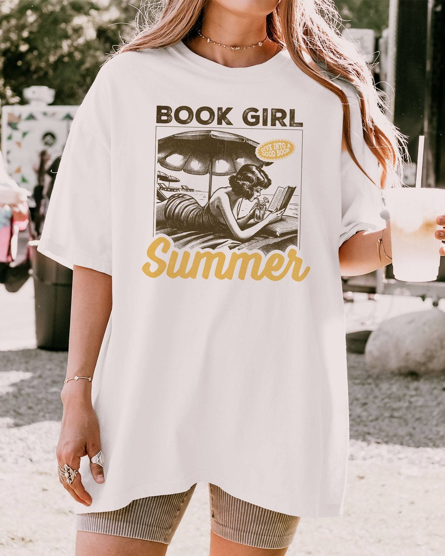 Woman wearing "Book Girl Summer" t-shirt in white color and with a retro graphic of a woman reading on a beach.