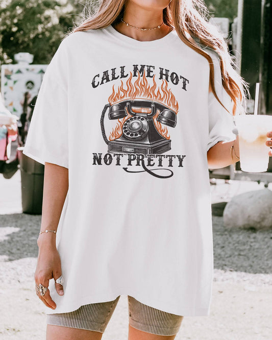 Woman wearing a white 'Call Me Hot Not Pretty' shirt with a retro graphic of a burning phone.