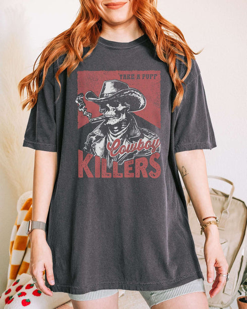 Woman wearing pepper color shirt with 'Cowboy Killers' funny smoking skeleton graphic design
