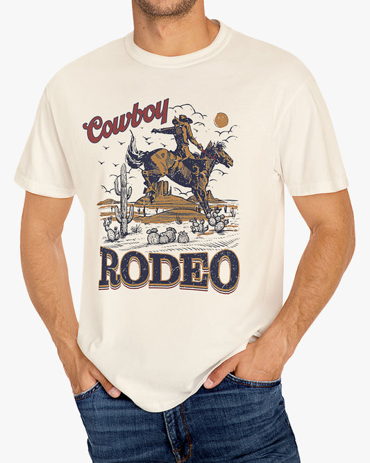 Man wearing a natural beige Cowboy Rodeo graphic t-shirt featuring a retro Western design, standing outdoors.