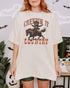 Woman wearing an ivory "Creepin It Country" shirt with a retro Halloween graphic of a pumpkin-headed cowboy riding a horse.