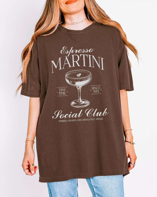Woman wearing an espresso-colored 'Espresso Martini Social Club – Stirred, Shaken, and Awake' shirt with a retro graphic of an espresso martini glass.