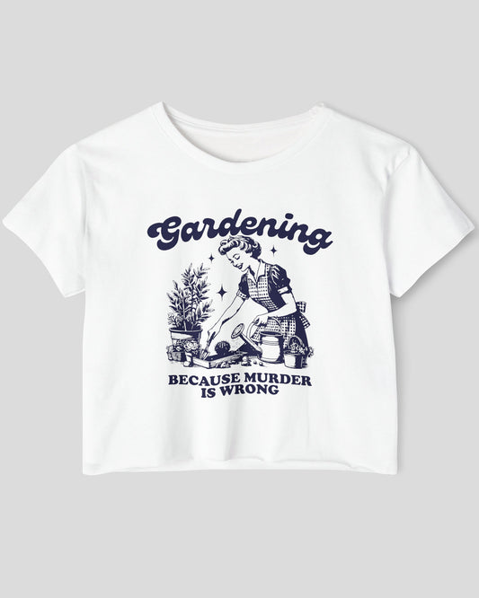 Flat-lay of a white crop top featuring a funny retro-style graphic of a housewife gardening with the text ‘Gardening, Because Murder Is Wrong’.