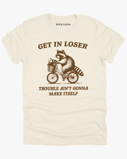 Flat lay natural 'Get In Loser, Trouble Ain't Gonna Make Itself' graphic tee featuring a funny retro raccoon riding a bicycle graphic.