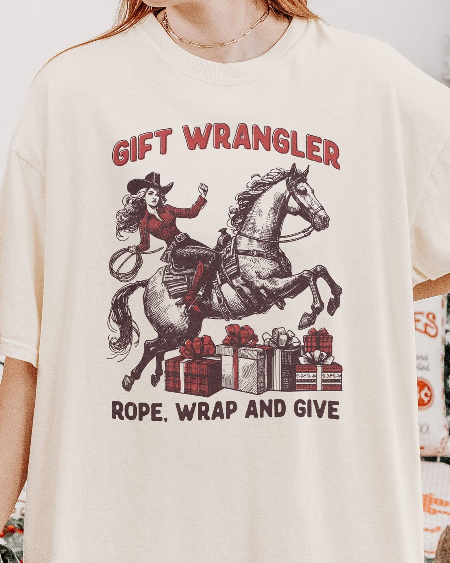 Close-up of woman wearing an ivory "Gift Wrangler – Rope, Wrap and Give" shirt with a funny retro cowgirl Christmas graphic.