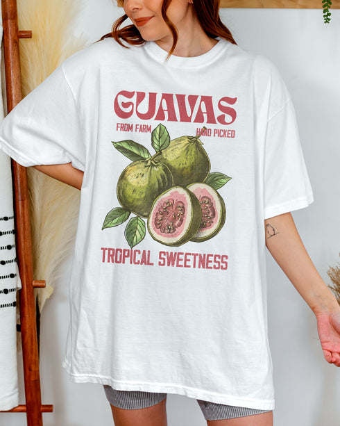Woman wearing a white "Guavas – Tropical Sweetness" shirt with a retro graphic of guava fruits.