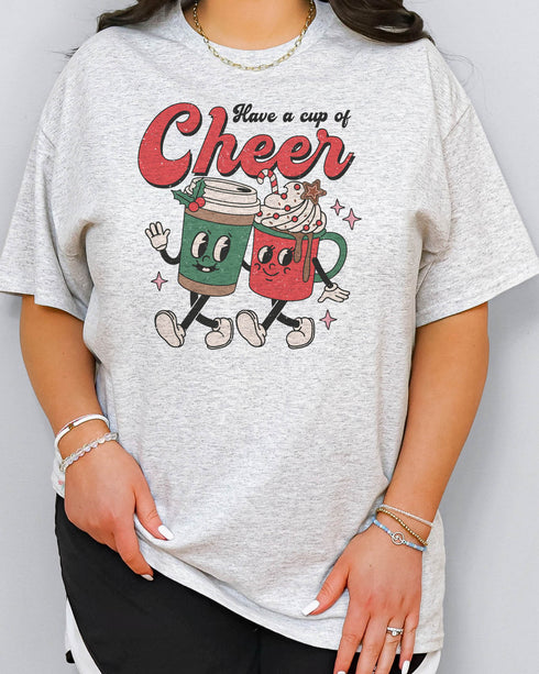 Woman wearing a retro Christmas coffee graphic shirt in ash grey color with the quote "Have A Cup of Cheer"