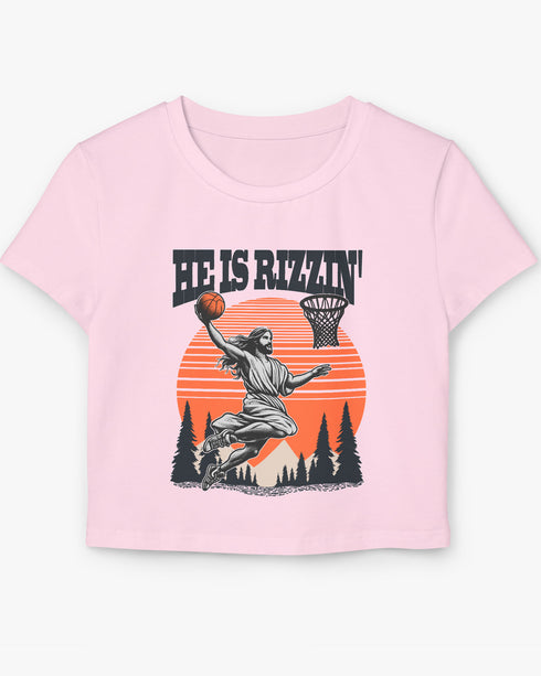 Woman wearing a light pink 'He Is Rizzin' baby tee featuring a funny retro Jesus playing basketball graphic, perfect for Y2K and Christian humor style.
