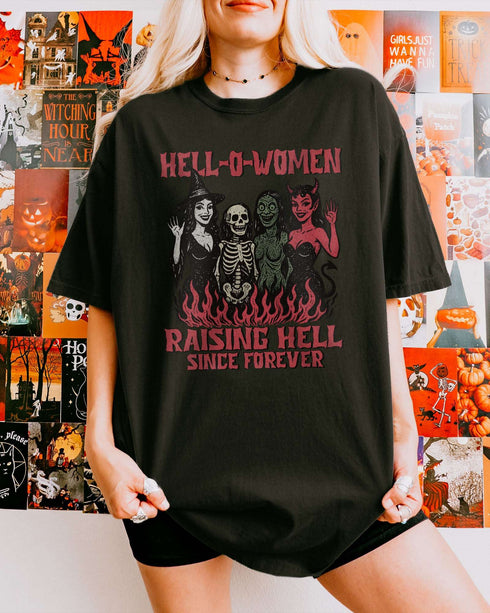 Woman wearing a black 'Hell-O-Women – Raising Hell Since Forever' shirt with a retro Halloween graphic of a witch, skeleton, zombie, and devil.