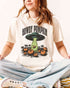 Woman wearing an ivory "Howdy Pumpkin" shirt with a retro graphic of a UFO abducting pumpkins from a field.