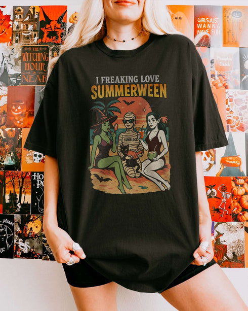 Woman wearing a black "I Freaking Love Summerween" shirt with a retro graphic of two witches and a mummy relaxing on the beach.