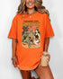 Woman wearing a burnt orange "I Freaking Love Summerween" shirt with a retro graphic of two witches and a mummy relaxing on the beach.
