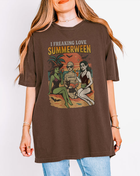 Woman wearing an espresso "I Freaking Love Summerween" shirt with a retro graphic of two witches and a mummy relaxing on the beach.