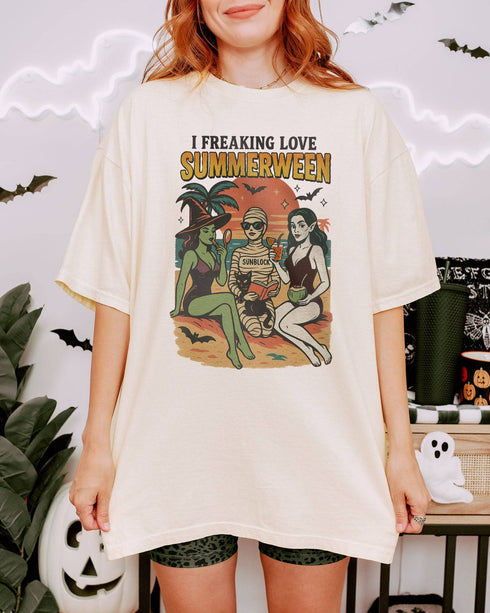 Woman wearing an ivory "I Freaking Love Summerween" shirt with a retro graphic of two witches and a mummy relaxing on the beach.