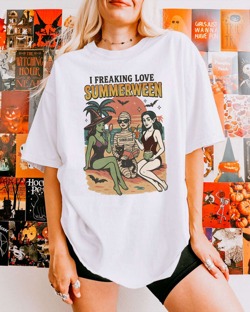 Woman wearing a white "I Freaking Love Summerween" shirt with a retro graphic of two witches and a mummy relaxing on the beach.