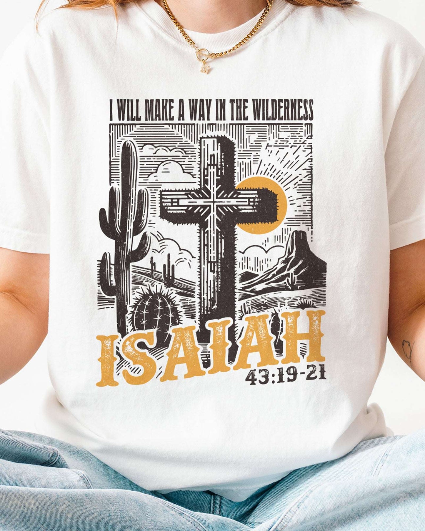 Close-up of woman wearing a white 'I Will Make a Way in the Wilderness – Isaiah 43:19-21' shirt with a retro graphic of a western desert and a Christian cross.