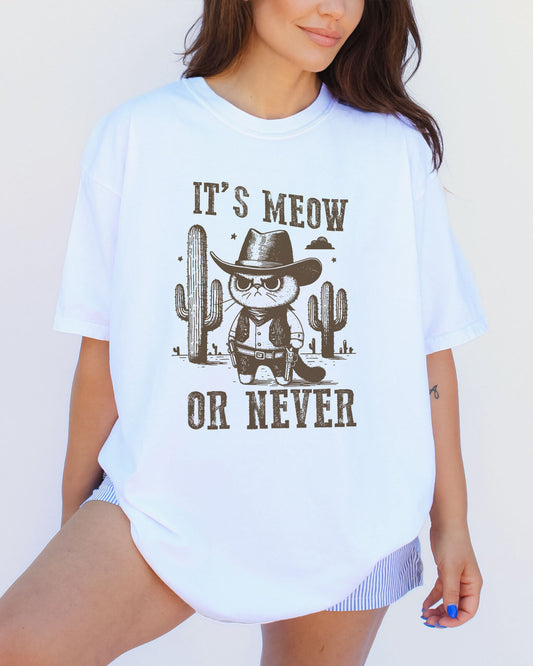 Model wearing white color shirt with 'It's Meow Or Never' cowboy cat graphic design