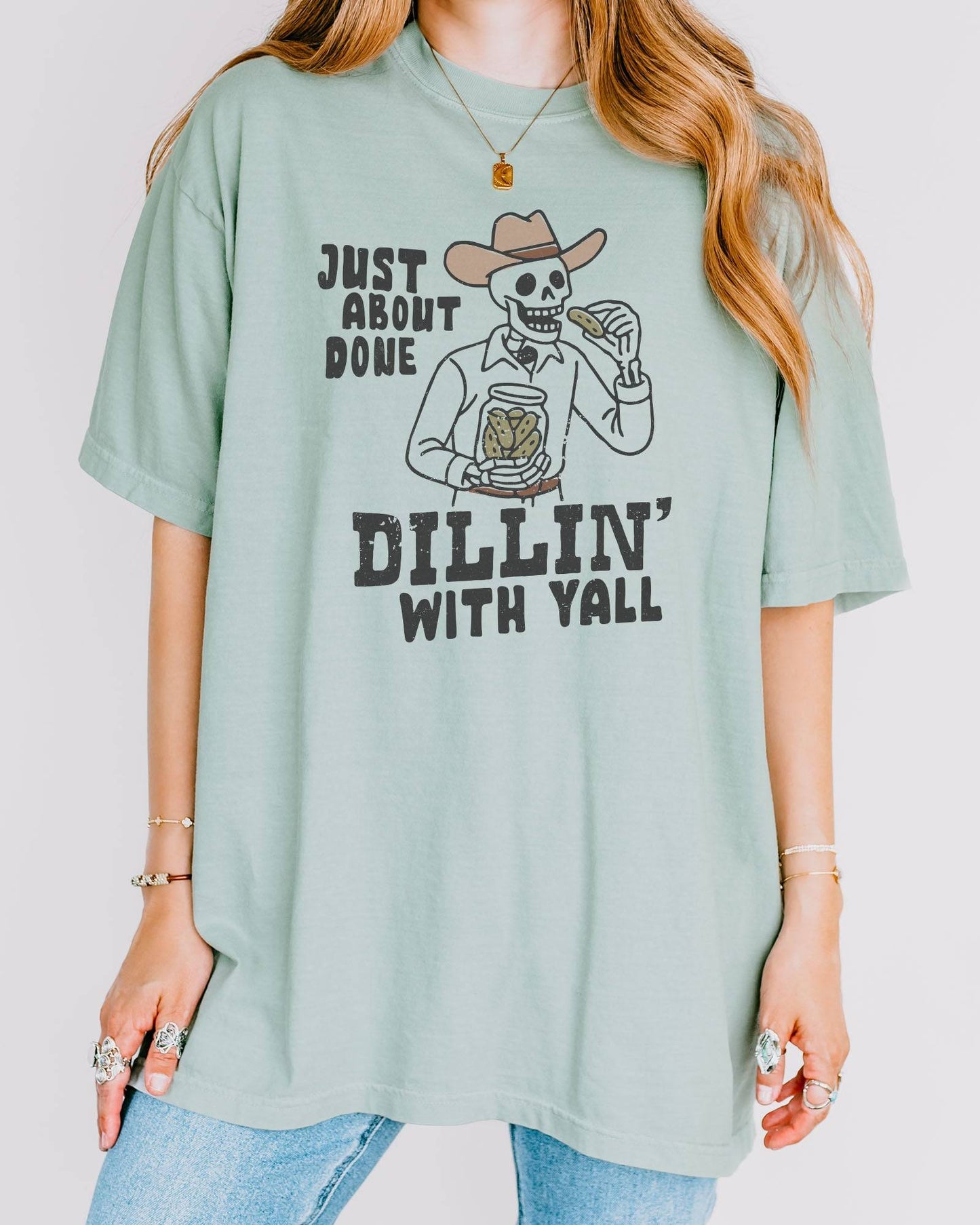 Model wearing bay color shirt with 'Just About Done Dillin With Yall' funny cowboy skeleton pickle graphic design