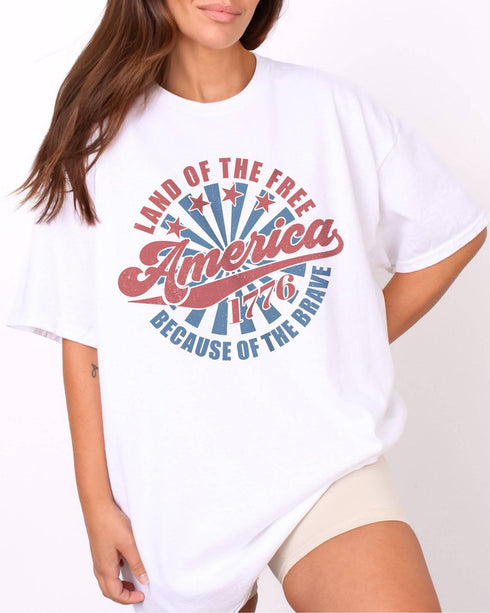 Model wearing white color shirt with 'Land Of The Free Because Of The Brave' graphic design