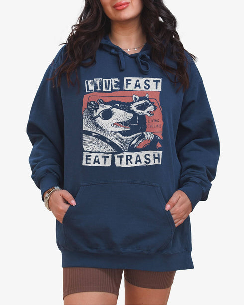 Woman wearing true navy 'Live Fast Eat Trash' hoodie with a funny retro graphic of two raccoons driving a car.