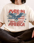 Close-up of man wearing "Made In America 1776" shirt in ivory color with retro graphic of a hawk in USA red-white-and-blue colors.