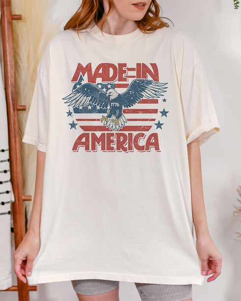 Woman wearing "Made In America 1776" shirt in ivory color with retro graphic of a hawk in USA red-white-and-blue colors.