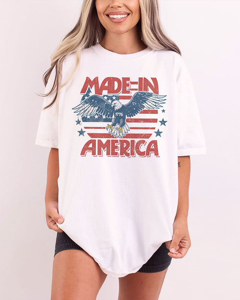 Woman wearing "Made In America 1776" shirt in white color with retro graphic of a hawk in USA red-white-and-blue colors.