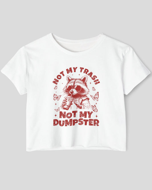 Flat lay of a white 'Not My Trash Not My Dumpster' crop top featuring a funny retro raccoon drinking coffee graphic.