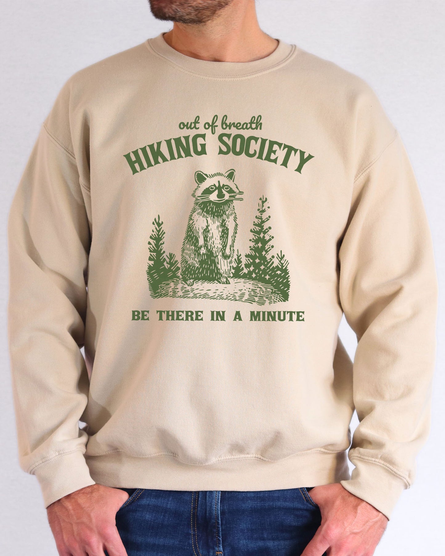 Model wearing sand color sweatshirt with 'Out Of Breath Hiking Society' graphic design