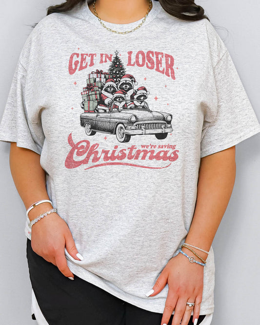 Woman wearing "Get In Loser We're Saving Christmas" shirt in ash grey color with a retro funny raccoon XMAS graphic