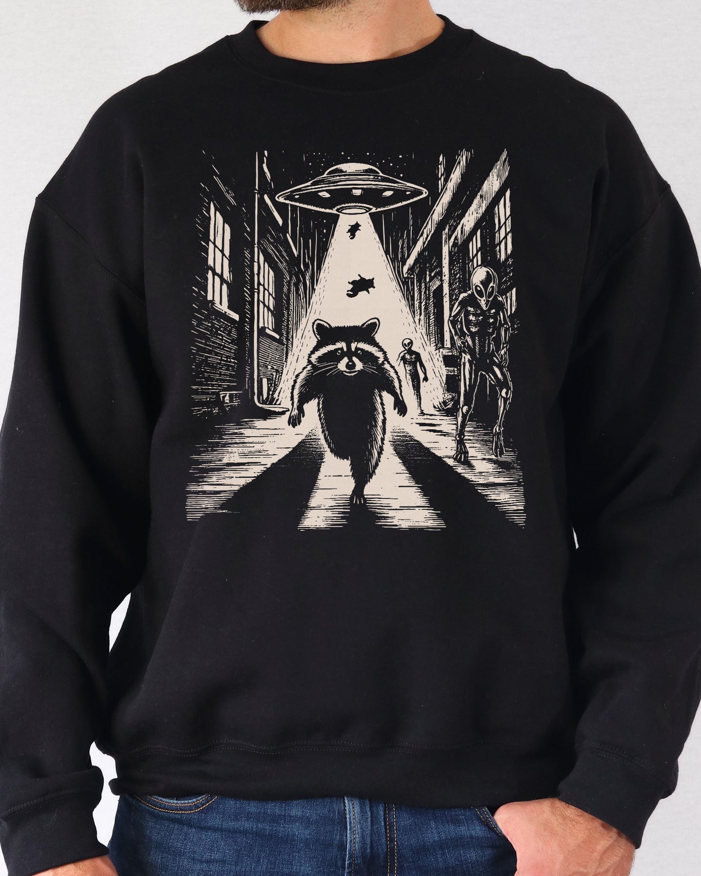 Man wearing a black sweatshirt with a retro graphic of a raccoon running from aliens.