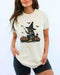 Model wearing ivory color shirt with 'Halloween Raccoon Witch' graphic design