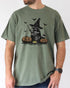 Model wearing moss color shirt with 'Halloween Raccoon Witch' graphic design