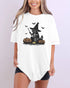 Model wearing white color shirt with 'Halloween Raccoon Witch' graphic design