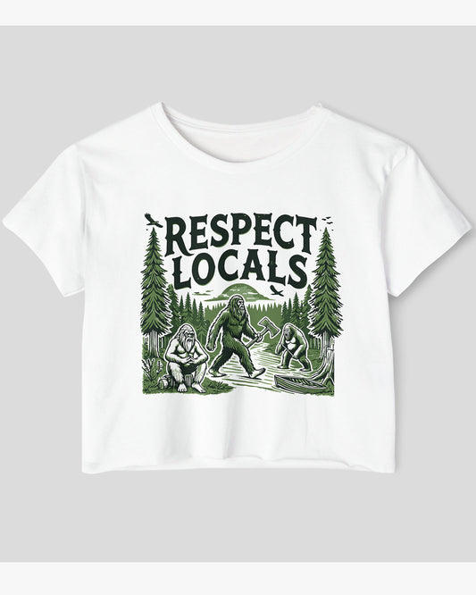 Flat-lay white 'Respect Locals' crop top featuring a funny retro Bigfoot walking through the forest graphic.