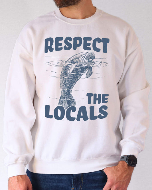 Man wearing a white sweatshirt with a retro manatee graphic and the text “Respect the Locals.”