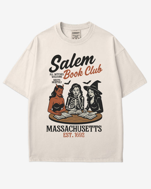 Flat lay ivory-colored 'Salem Book Club Massachusetts 1692' shirt with retro Halloween graphic of a devil, skeleton, and witch sitting together reading at a table.