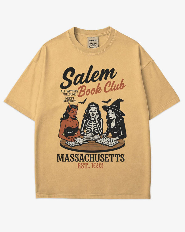 Flat lay mustard-colored 'Salem Book Club Massachusetts 1692' shirt with retro Halloween graphic of a devil, skeleton, and witch sitting together reading at a table.