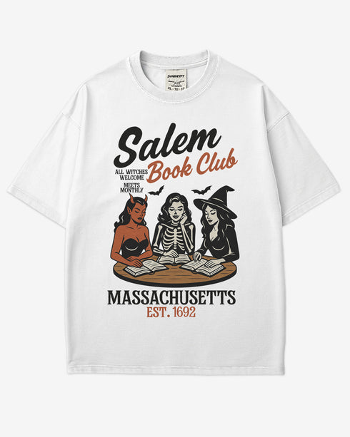 Flat lay white-colored 'Salem Book Club Massachusetts 1692' shirt with retro Halloween graphic of a devil, skeleton, and witch sitting together reading at a table.