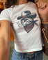 Woman wearing white baby tee with retro graphic of smoking cowboy cat