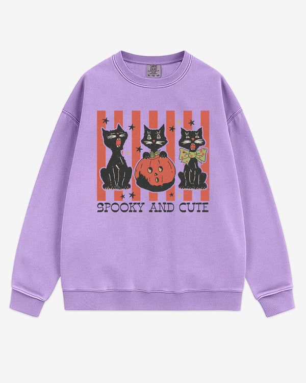 Flat lay orchid-colored 'Spooky And Cute' sweatshirt with retro Halloween graphic of three black cats and a pumpkin.