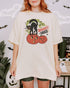 Woman wearing an ivory "Spooky Vibes" shirt with a retro Halloween graphic of a black cat hissing on two pumpkins.