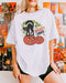 Woman wearing a white "Spooky Vibes" shirt with a retro Halloween graphic of a black cat hissing on two pumpkins.