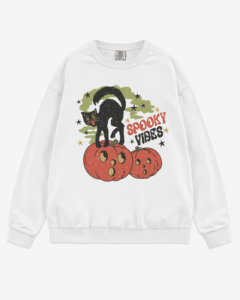 Flat lay white Halloween sweatshirt reading โSpooky Vibesโ with retro graphic of black cat standing on pumpkins.
