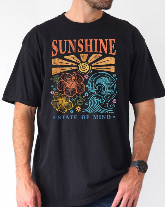 Man wearing a black "Sunshine State of Mind" shirt with a retro graphic of outlined flowers, sun, and waves.